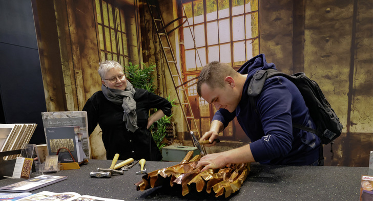 Ein Messebesucher versucht unter Anleitung der Künstlerin Manuela Geugelin Kupferkunst anzufertigen - © Bild: BAUMETALL

